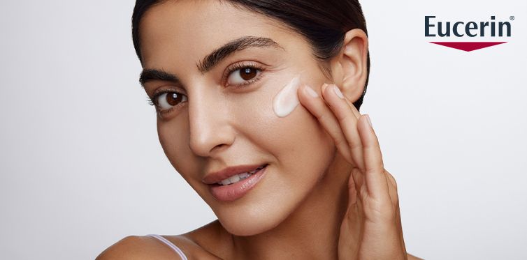 Mörkhårig kvinna smörjer in sitt ansikte med produkt från varumärket Eucerin.